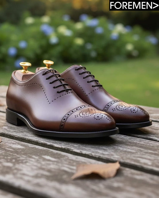 Brown dress shoes on a wooden surface with a blurred natural background
